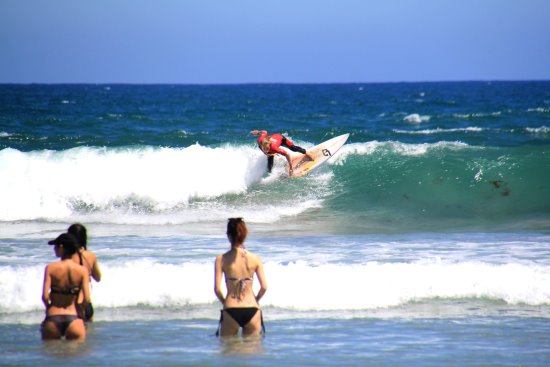 Two swimmers watching a surfer at the beach.
