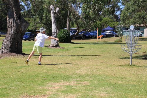 A child throwing a frisbee golf disc into a metal basket. A young boy playing frisbee golf.